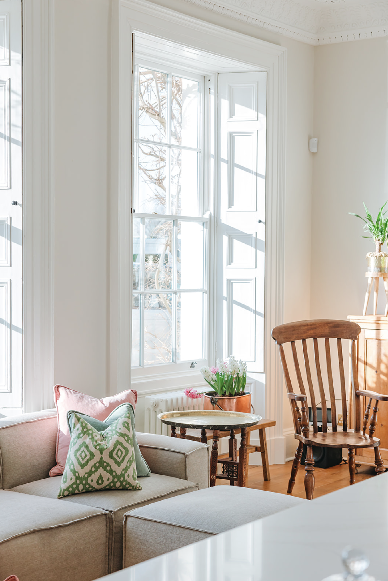 Sitting room bay with tall sash windows, working shutters and a Windsor chair beside a copper planter