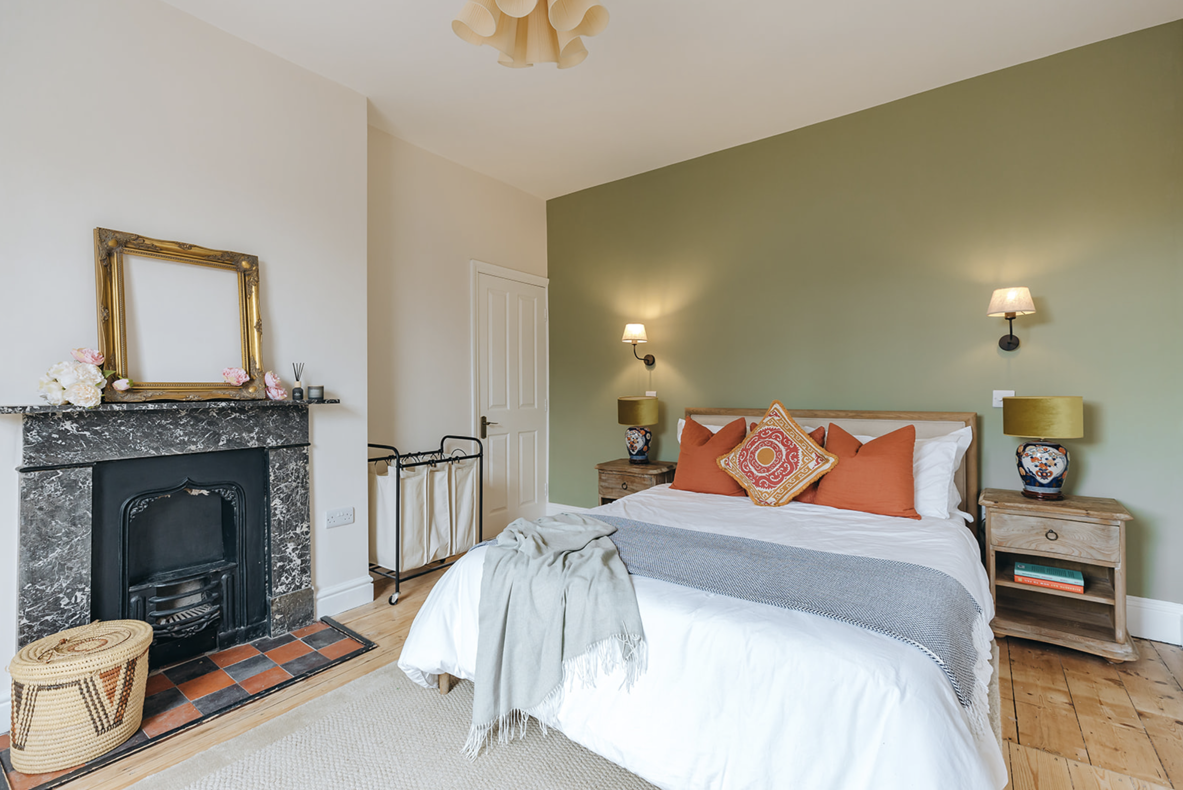 Bedroom with a green accent wall, retained grey marble fireplace with cast-iron insert and a chequered tiled hearth