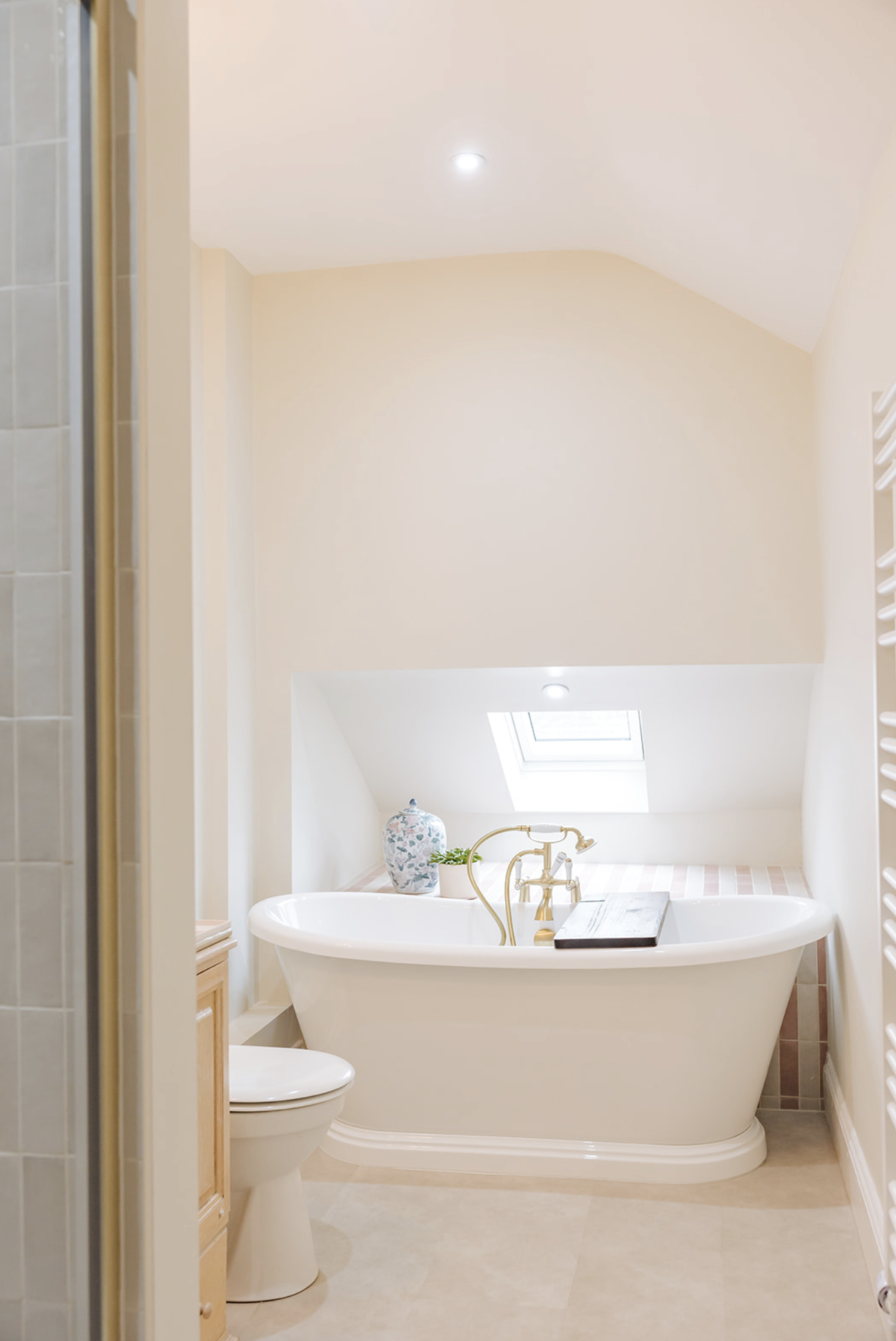 Attic bathroom with freestanding bath and brass mixer beneath a skylight