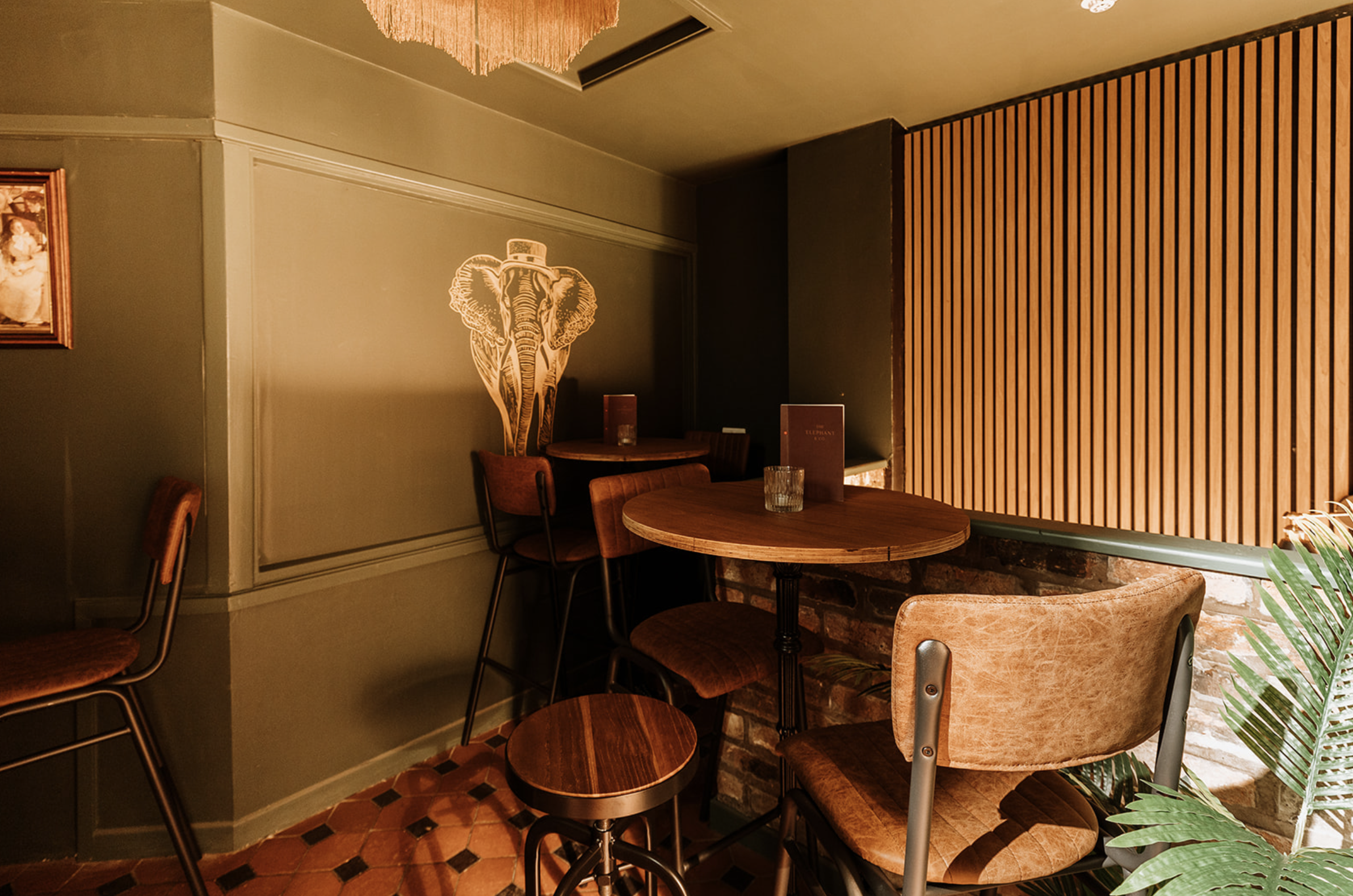 Green panelled snug at The Underground with slatted timber wall, fringed pendant and the gold elephant motif