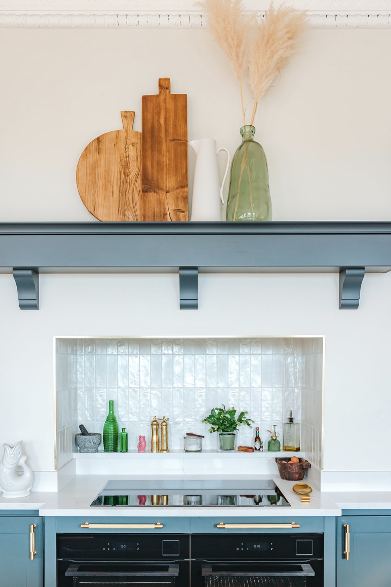 Teal cooking wall with a white tiled niche, twin ovens, brass rail and styled timber boards