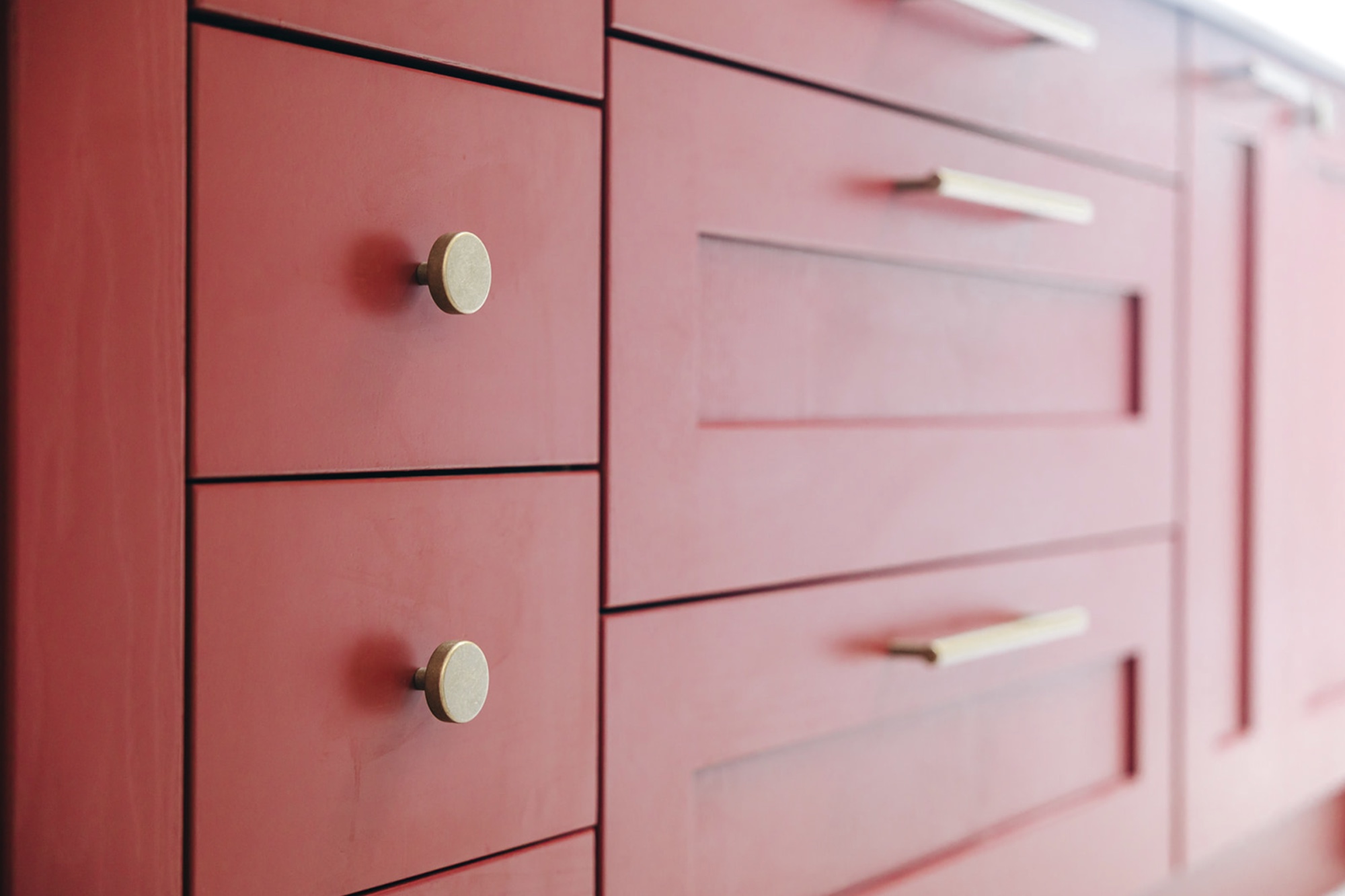 Close view along the rust-red hand-painted kitchen island with round brass knobs