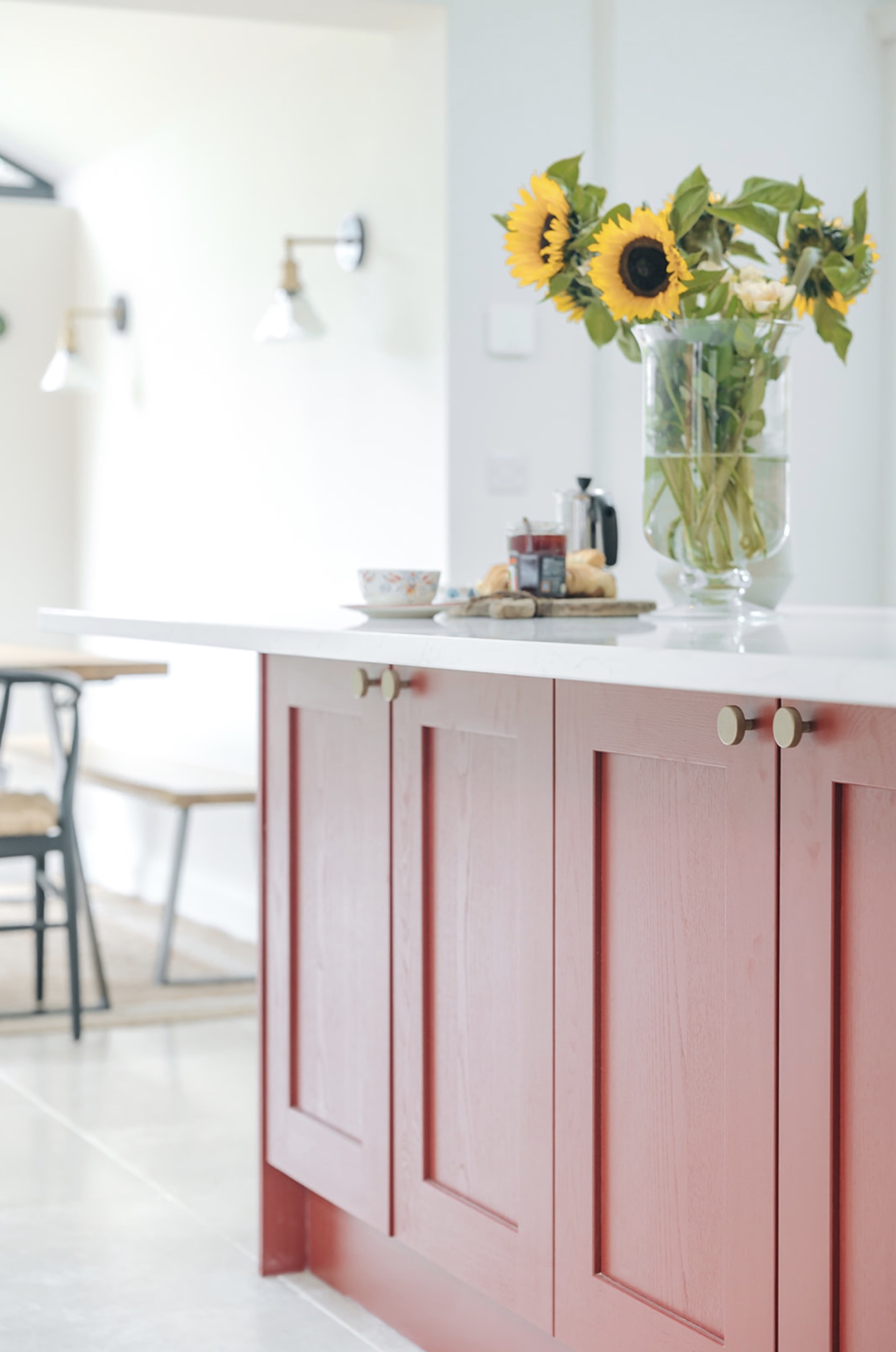 Rust-red kitchen island with a white worktop, brass knobs, breakfast setting and sunflowers