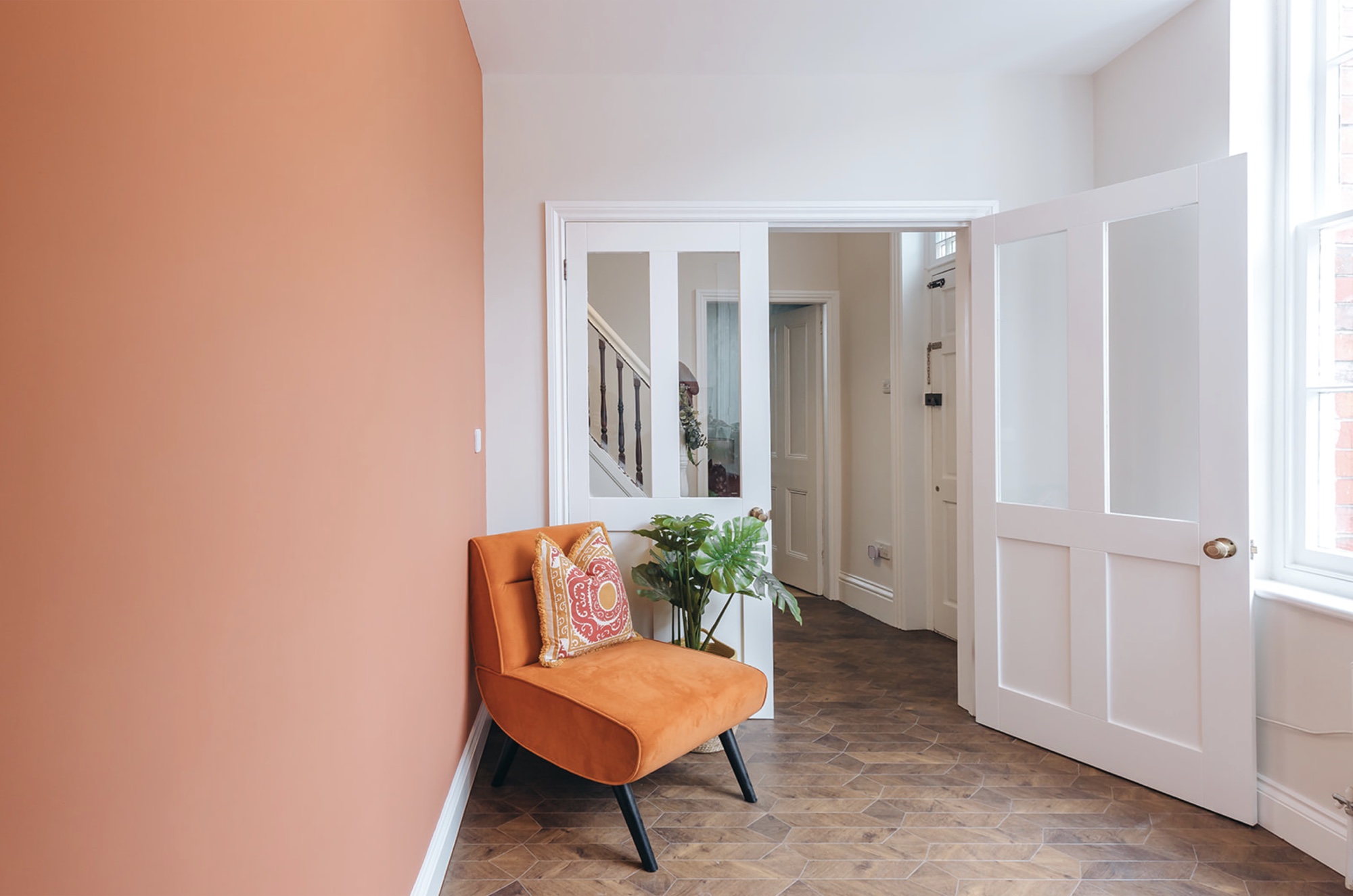 Terracotta-painted room with orange chair, glazed doors to the entrance hall and a herringbone floor