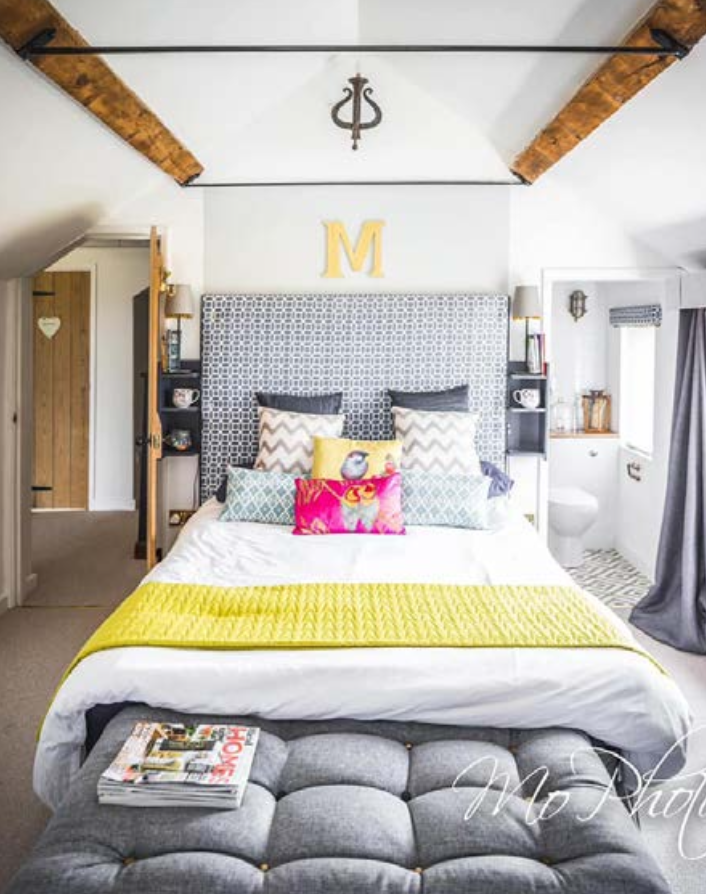 Mount Pleasant principal bedroom under a vaulted beamed ceiling, with an upholstered headboard, bedside niches and an en-suite through the opening beyond