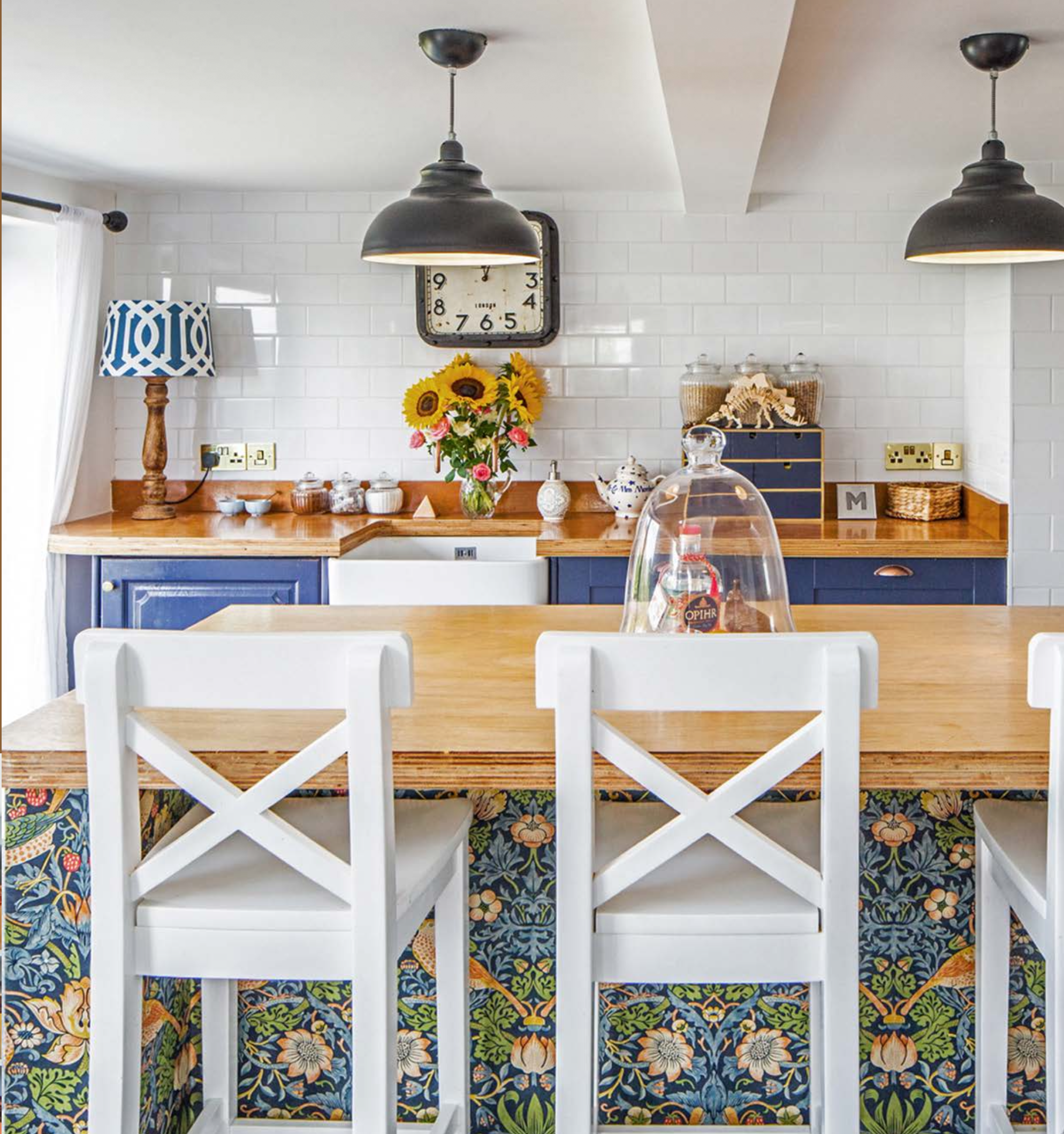Mount Pleasant kitchen: navy cabinetry with plywood worktops, white metro tiling, butler sink, industrial pendants and a breakfast bar faced in William Morris Strawberry Thief