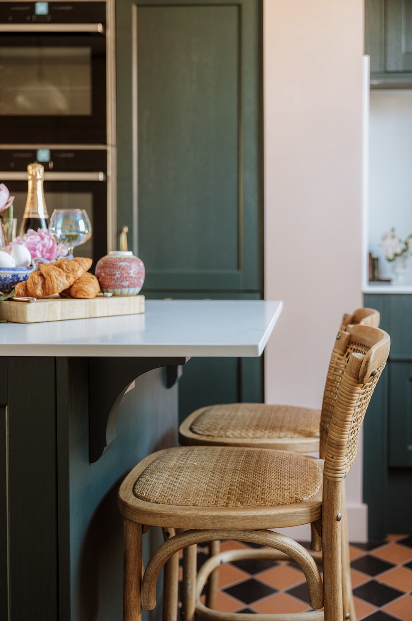 Woven timber stools tucked beneath the green kitchen island