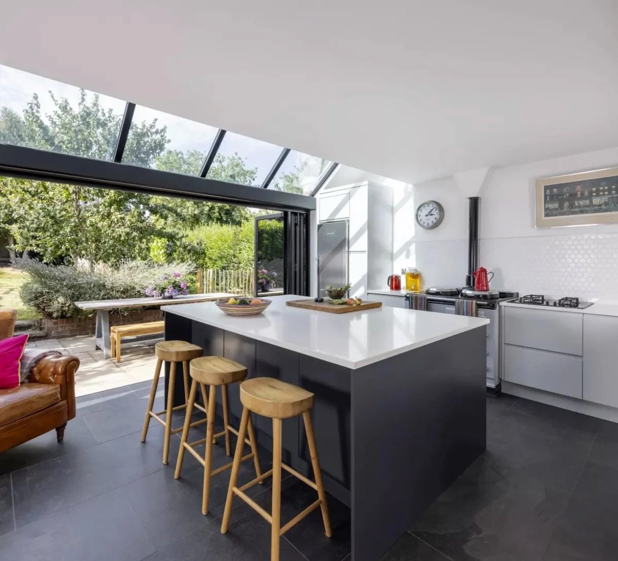Interior of the Oakleigh House extension: kitchen island beneath the glazed roof with folding doors open to the garden