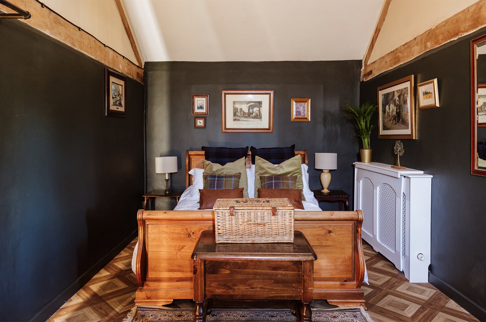 The Pool House bedroom with dark walls, exposed timber beams and a warm timber bed