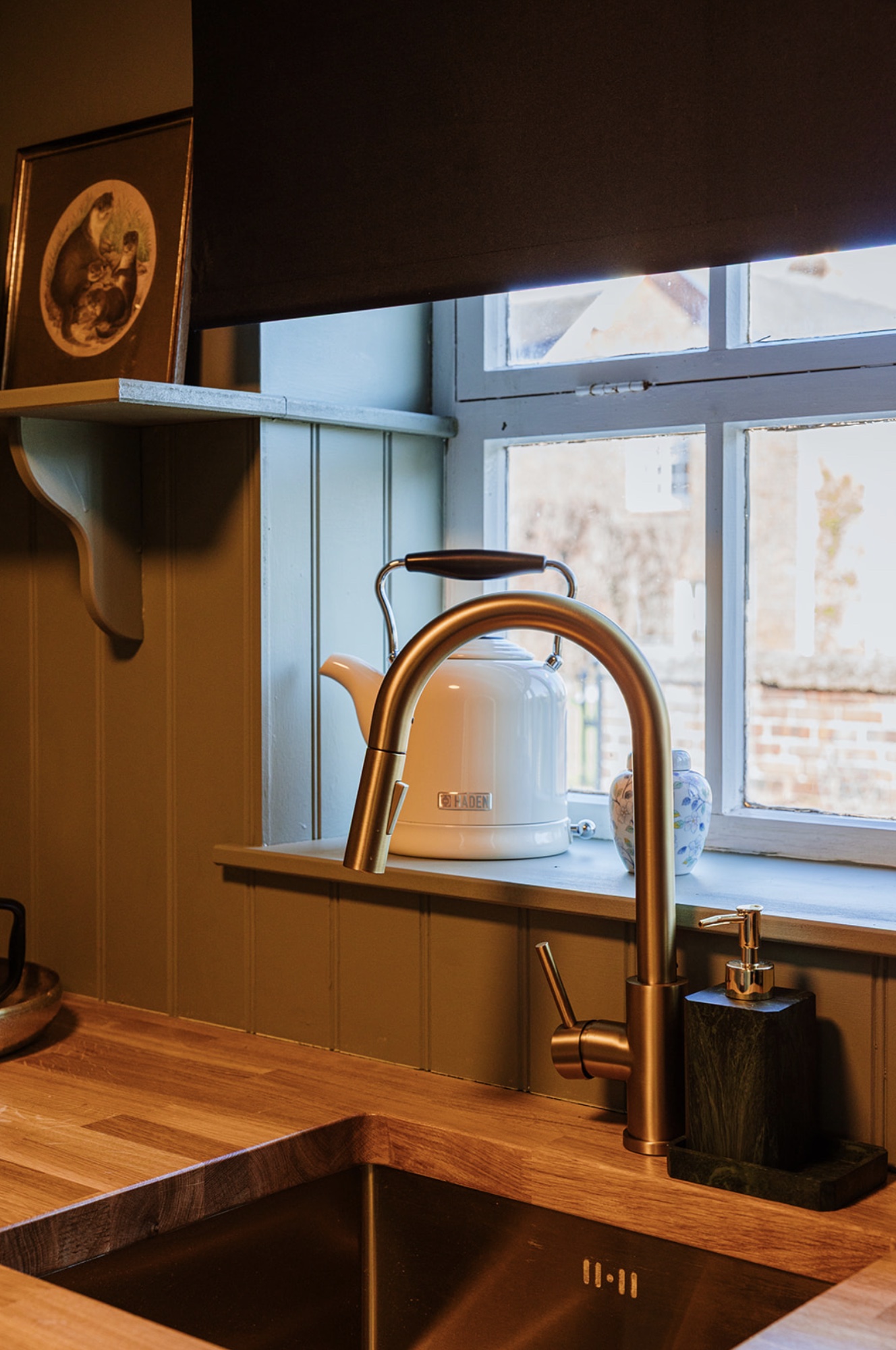 Brushed brass kitchen tap, timber worktop and white kettle beside the Pool House window